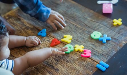From above of crop anonymous ethnic baby and kid playing with assorted toy numbers and letters at wooden table in house