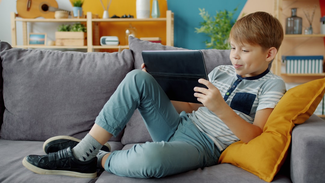 Young boy watches tablet while relaxing on couch.