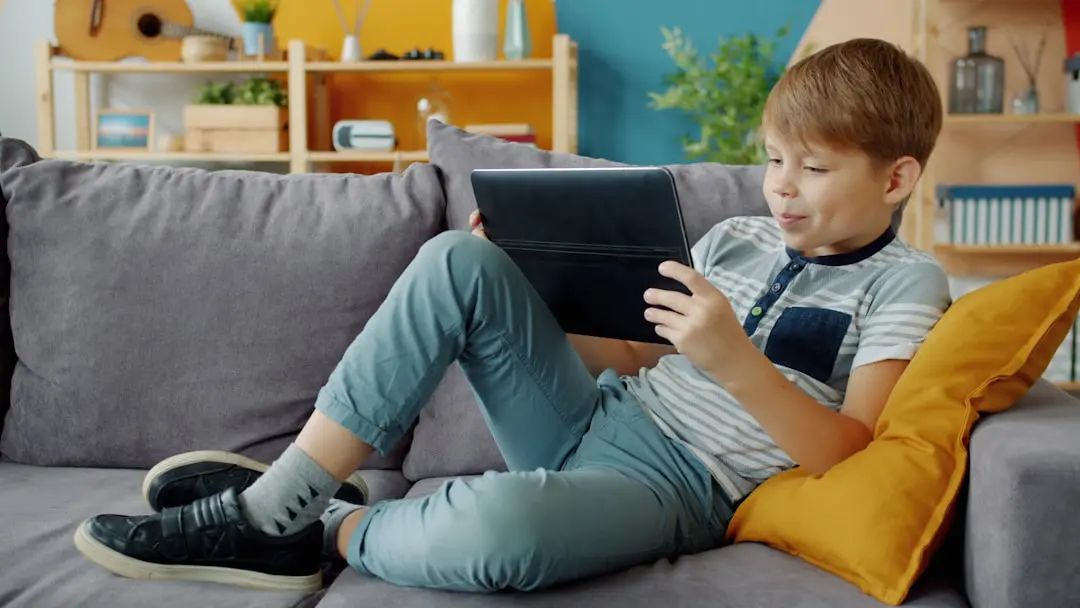 Young boy watches tablet while relaxing on couch.